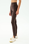 A person wears SPLITS59's River High Waist Airweight Stirrup leggings in Dark Chocolate with white athletic shoes, standing against a plain white background.