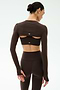 A woman stands with her back to the camera in SPLITS59’s Amelia Airweight Lite Shrug in Dark Chocolate, featuring long sleeves and back cutouts, paired with matching high-waisted leggings—ideal for yoga or dance.