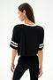 A woman faces away in the SPLITS59 Djuna Oversized Crop Jersey Tee - Black/Creme, paired with striped black leggings, against a plain white background.