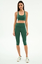 A woman faces forward against a white backdrop, wearing the SPLITS59 Ella Airweight Bra in Arugula/White with high-waisted leggings and white striped sneakers.