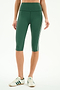 A person wearing SPLITS59 Ella High Waist Airweight Capri in Arugula/White, paired with white Adidas sneakers, stands against a plain background.