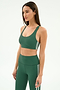 A woman wears the SPLITS59 Ella Airweight Bra in Arugula/White, paired with high-waisted leggings featuring white side stripes, made from soft nylon spandex stretch fabric, standing against a plain light background.