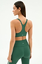 A woman models the SPLITS59 Ella Airweight Bra in Arugula/White, facing away to highlight its racerback design and seamless nylon-spandex fit against a plain white background.