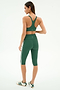 A woman stands facing away in SPLITS59’s Ella Airweight Bra - Arugula/White, paired with matching leggings and white sneakers with green stripes, against a plain white background.