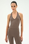 A person stands against a white background, wearing the SPLITS59 June Rib Halter in Lentil—a sleeveless brown halter-neck top—paired with matching high-waisted leggings, both crafted from stretchy material for a comfortable and flattering fit.
