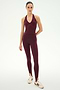 A woman stands against a plain background, wearing the SPLITS59 June Rib Halter in Dark Cherry and matching leggings crafted from a soft modal spandex blend, styled with beige sneakers featuring burgundy stripes.