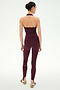A woman stands facing away, wearing the SPLITS59 June Rib Halter in Dark Cherry and matching leggings crafted from a soft modal spandex blend, paired with sandals. Her hair is tied back against a plain white background.