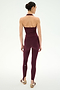 A woman stands facing away, wearing the SPLITS59 June Rib Halter in Dark Cherry and matching leggings crafted from a soft modal spandex blend, paired with sandals. Her hair is tied back against a plain white background.