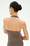 A woman with dark hair in a bun is seen from behind against a plain, light background, wearing the SPLITS59 June Rib Halter in Lentil—a taupe halter-style top crafted from soft modal fabric.