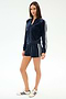 A woman stands wearing the SPLITS59 Heritage Velour Bomber in indigo/white, styled with matching shorts and white sneakers featuring dark stripes.