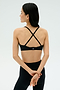 A woman stands with her back to the camera, arms crossed, wearing the SPLITS59 Theo Rigor Bra - Black and leggings—ideal for multisport performance thanks to its super soft Rigor fabric.