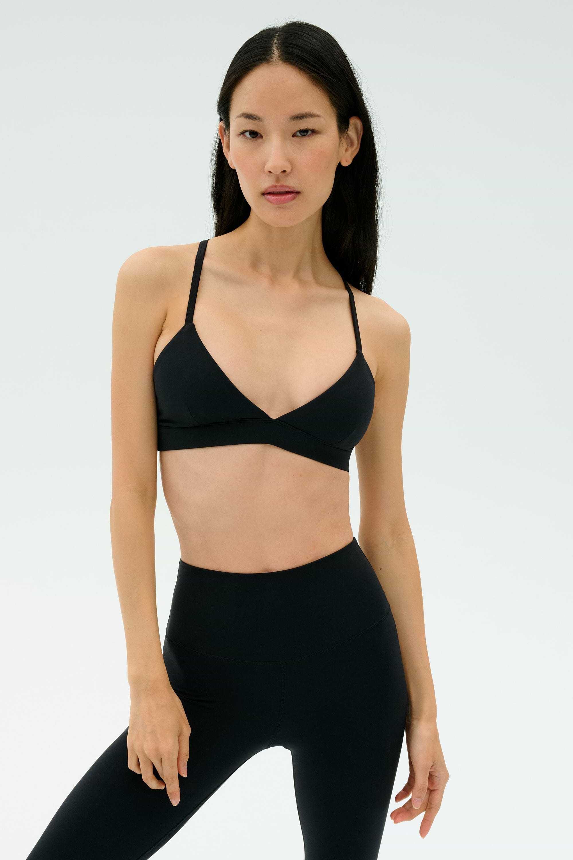 Woman stands against a plain background, wearing the SPLITS59 Theo Rigor Bra - Black and high-waisted black leggings, both crafted from ultra luxe Rigor fabric for multi-sport performance.
