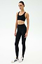 A person stands facing forward wearing the SPLITS59 River High Waist Airweight Stirrup leggings in black with white sneakers, set against a plain light background.
