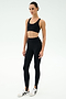 A person stands facing forward wearing the SPLITS59 River High Waist Airweight Stirrup leggings in black with white sneakers, set against a plain light background.