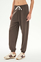A person wearing the SPLITS59 Andie Oversized Fleece Sweatpant in Lentil, featuring a soft fleecy finish and a white drawstring, paired with beige sneakers with maroon stripes, stands against a plain light background.