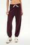 A person stands against a white background wearing SPLITS59′s Andie Oversized Fleece Sweatpant in Dark Cherry—crafted from ultra-luxe fleece and made in Los Angeles—paired with beige sneakers featuring burgundy stripes and a white drawstring; ideal for cool weather workouts.