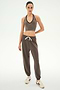 A woman stands facing forward against a plain white background, wearing SPLITS59 Andie Oversized Fleece Sweatpant in Lentil with a brown halter crop top and white sneakers.