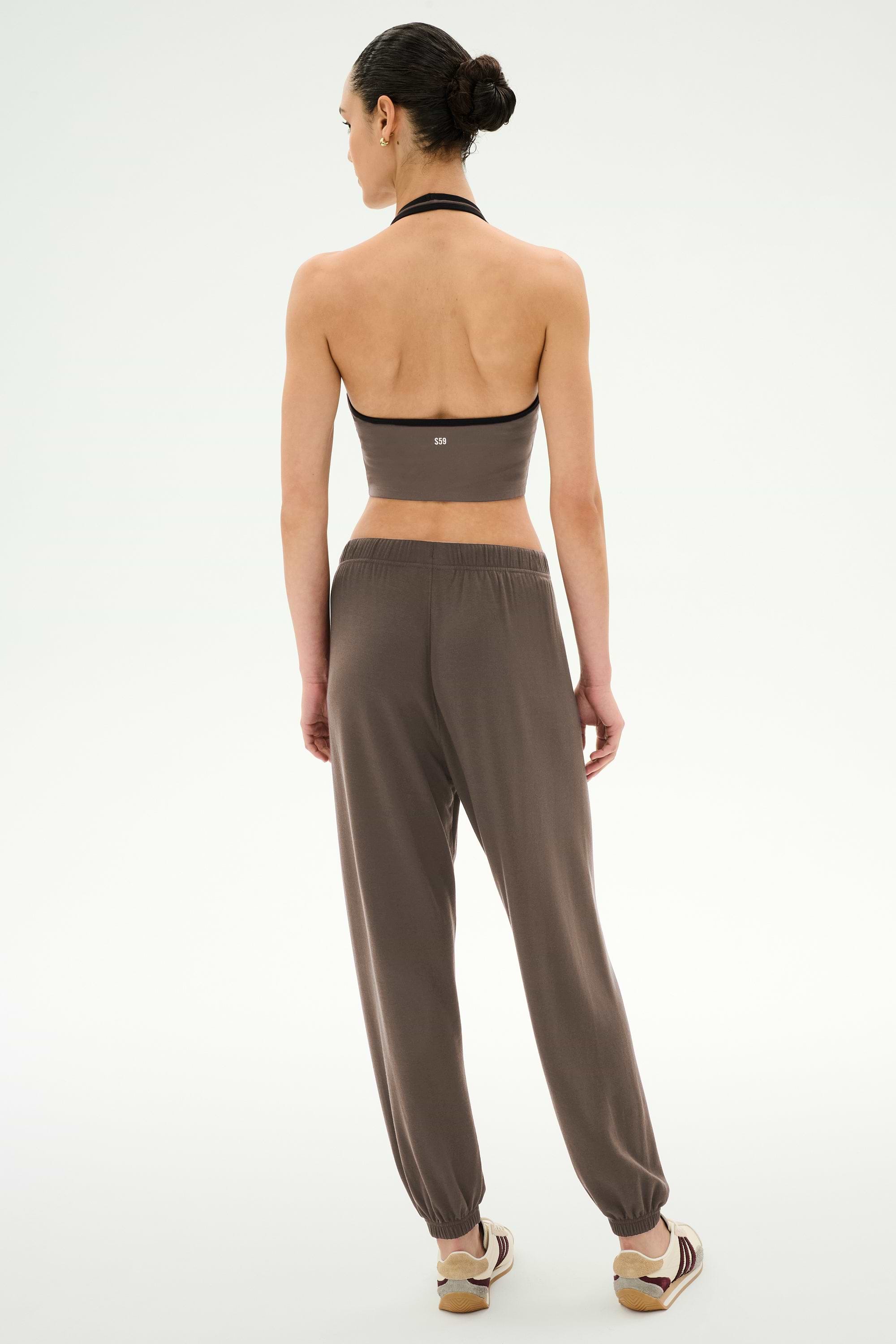 A woman stands facing away against a plain light background, wearing the SPLITS59 Andie Oversized Fleece Sweatpant in Lentil, styled with a strapless dark crop top and beige sandals.