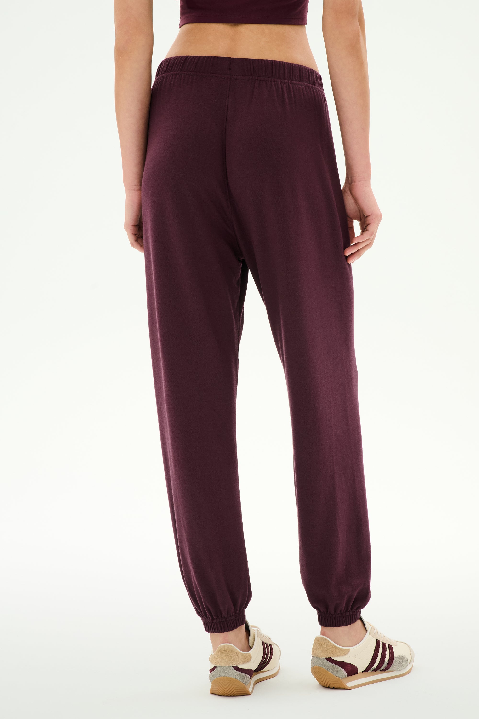 Model is shown from the back wearing SPLITS59 Andie Oversized Fleece Sweatpant in Dark Cherry with sneakers, standing against a plain white background—ideal for cool weather workouts.