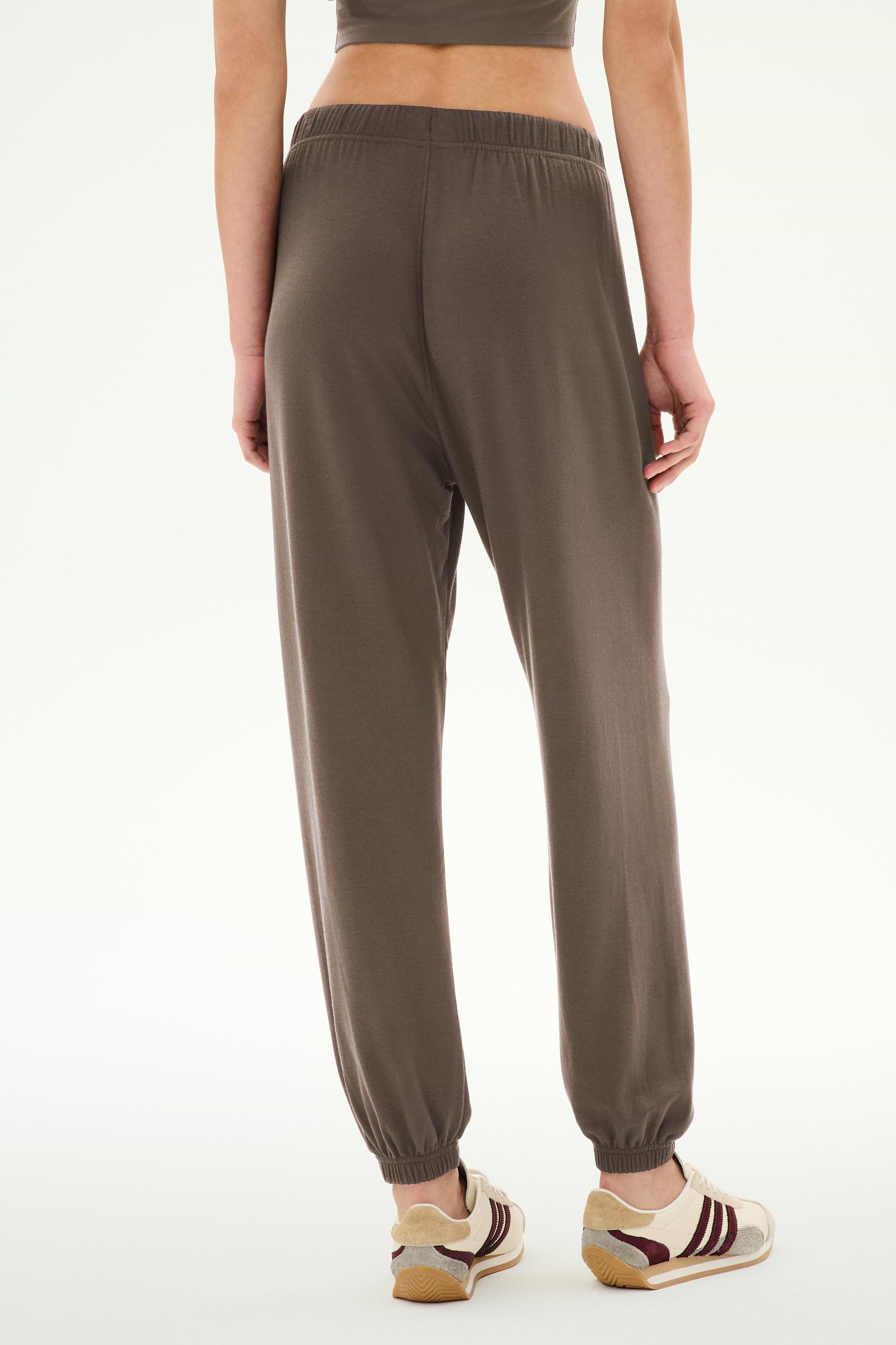 A person wearing the SPLITS59 Andie Oversized Fleece Sweatpant in Lentil, paired with striped sneakers, is shown from the back against a plain white background.