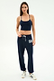 A woman stands against a plain white background, wearing a navy crop top, white sneakers, and SPLITS59 Andie Oversized Fleece Varsity 59 Sweatpant in Indigo/59 with “59” on the left leg.