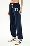 A person wears the SPLITS59 Andie Oversized Fleece Varsity 59 Sweatpant in Indigo/59, paired with white sneakers with navy stripes, standing against a white background. Made in Los Angeles.