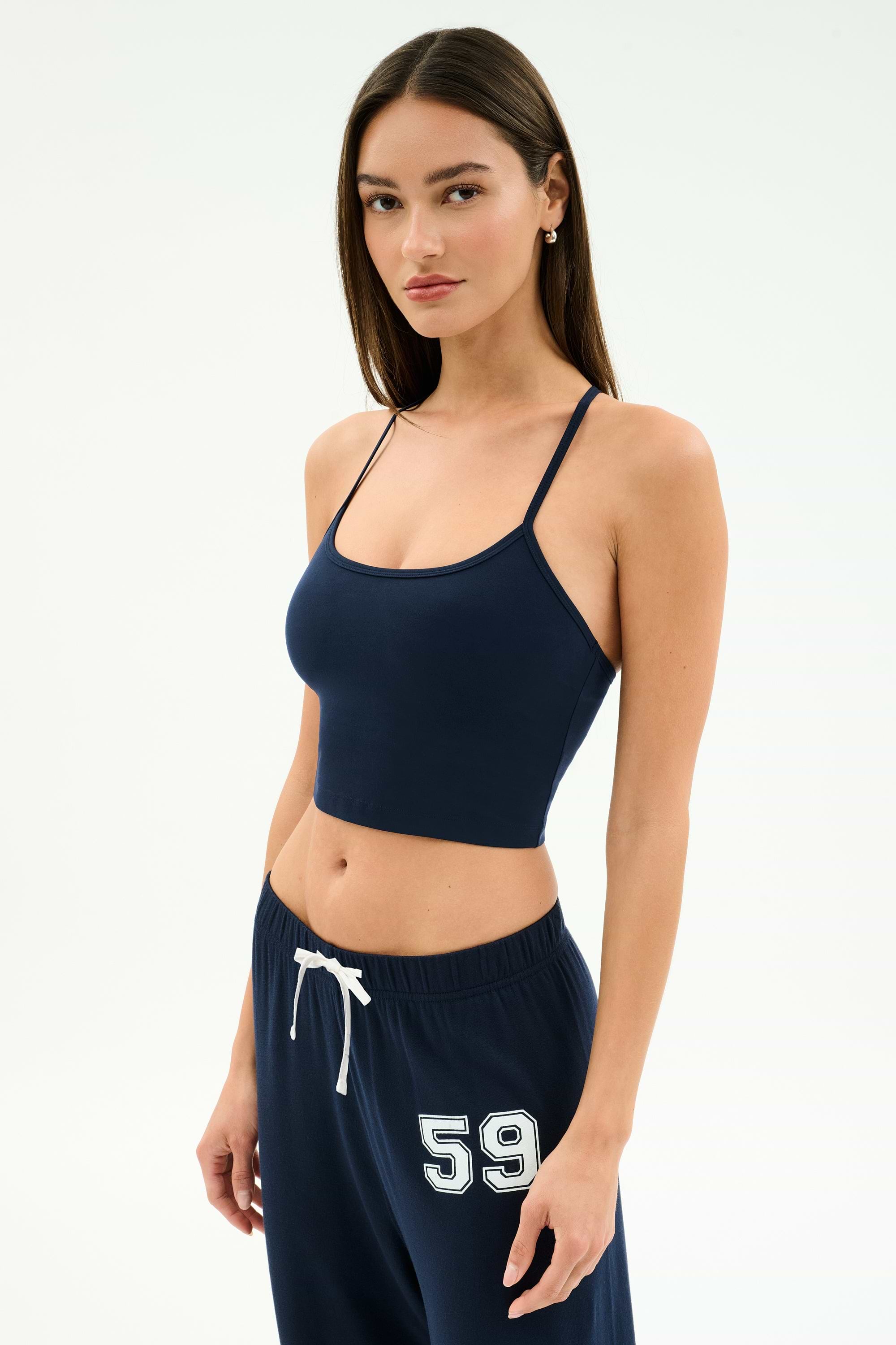 A woman stands against a plain background wearing the SPLITS59 Airweight Crop - Indigo and matching indigo sweatpants with "59" on the hip—ideal for hot yoga or relaxed, casual days.