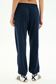 Model stands against a white background, shown from the back, wearing SPLITS59 Andie Oversized Fleece Varsity 59 Sweatpant in Indigo/59 and white sneakers with blue stripes. Made in Los Angeles.