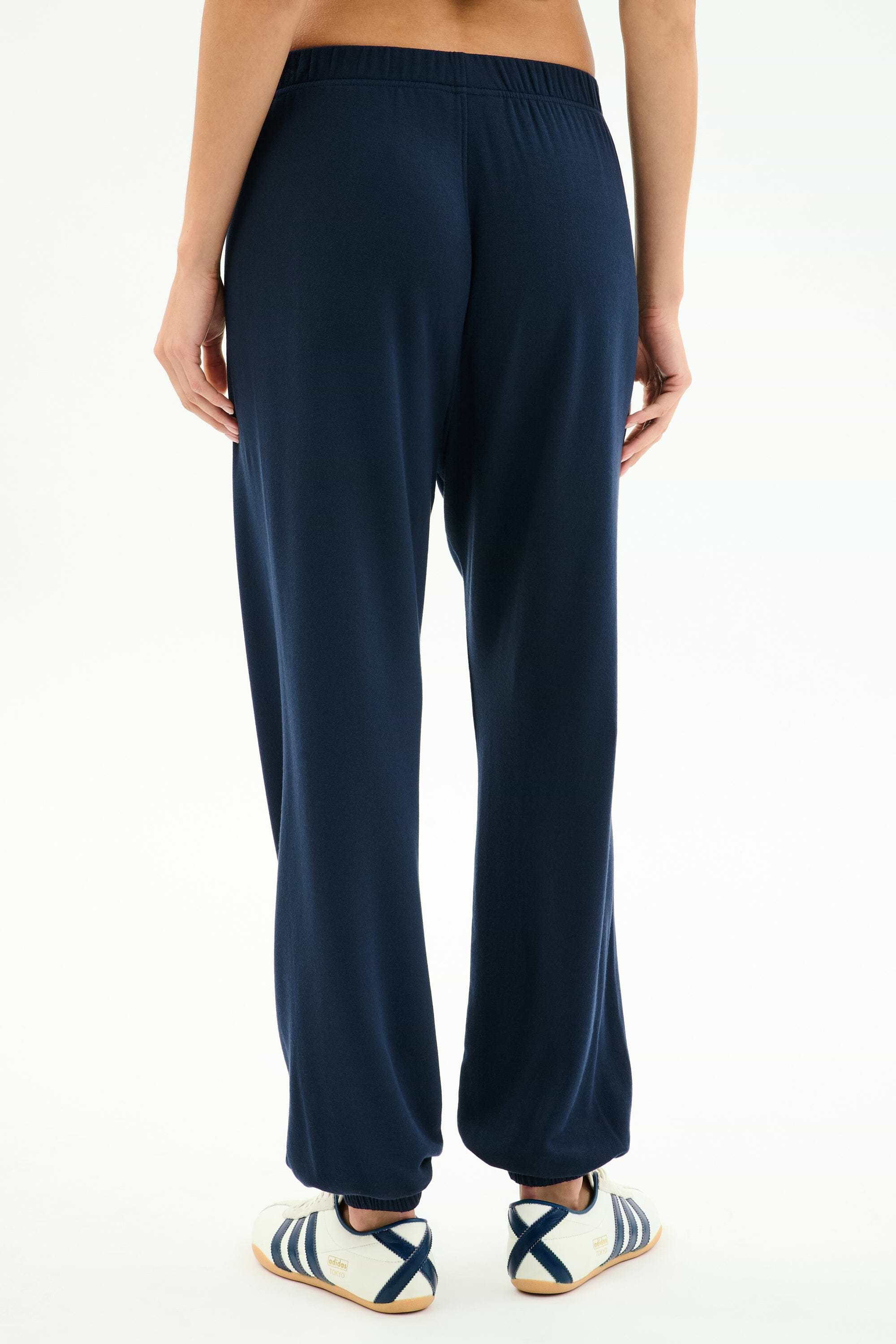 Model stands against a white background, shown from the back, wearing SPLITS59 Andie Oversized Fleece Varsity 59 Sweatpant in Indigo/59 and white sneakers with blue stripes. Made in Los Angeles.