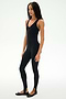 A person stands against a plain background wearing the SPLITS59 Darci Airweight Stirrup Jumpsuit in black, a form-fitting, stretch, sleeveless one-piece with stirrup legs, paired with black ballet flats.