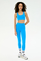 A woman wearing the SPLITS59 Ella Airweight Bra in Riviera/White, matching leggings, white sneakers, and white socks stands against a plain white background.