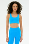 A woman with curly hair wears the SPLITS59 Ella Airweight Bra in Riviera/White and matching leggings, standing against a plain white background.