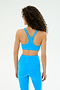 A woman with curly hair, seen from behind, wears the SPLITS59 Ella Airweight Bra in Riviera/White and matching leggings, standing against a plain light background.