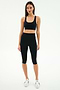 A woman stands against a plain background wearing the SPLITS59 Ella High Waist Airweight Capri in Black/White, a black sports bra, and white sneakers.