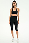 A woman stands against a plain background wearing the SPLITS59 Ella High Waist Airweight Capri in Black/White, a black sports bra, and white sneakers.