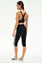 A woman stands in a three-quarter pose wearing the SPLITS59 Ella High Waist Airweight Capri in Black/White and a black sports bra with white sneakers against a plain background.