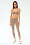 A woman stands against a plain background wearing the SPLITS59 Mia Rigor Legging w/ Stripe in Latte/White, paired with a taupe sports bra and beige sneakers.
