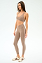 A woman wears SPLITS59's Mia Rigor Legging w/ Stripe in Latte/White with a taupe sports bra and white sneakers with brown accents, standing against a plain white background.
