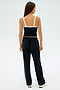 An individual is dressed in a black SPLITS59 sports top featuring white straps, paired with Maxie Rigor Track Pant - Black/White from SPLITS59, standing against a light background.