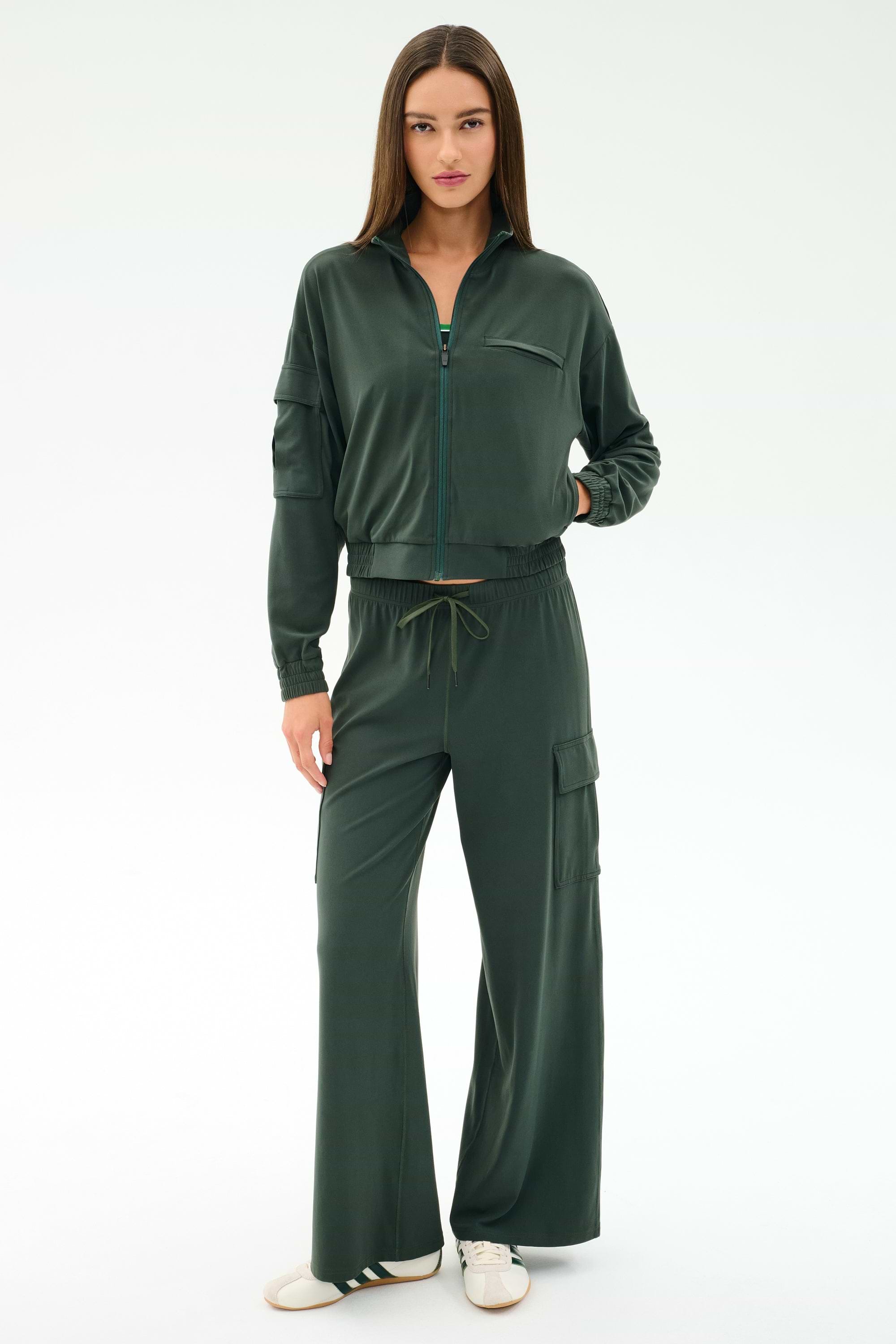 A woman stands facing forward, wearing the SPLITS59 Peaches Airweight Cargo Jacket in Military with matching wide-leg cargo pants, both crafted from soft nylon spandex, paired with white sneakers against a plain light background.