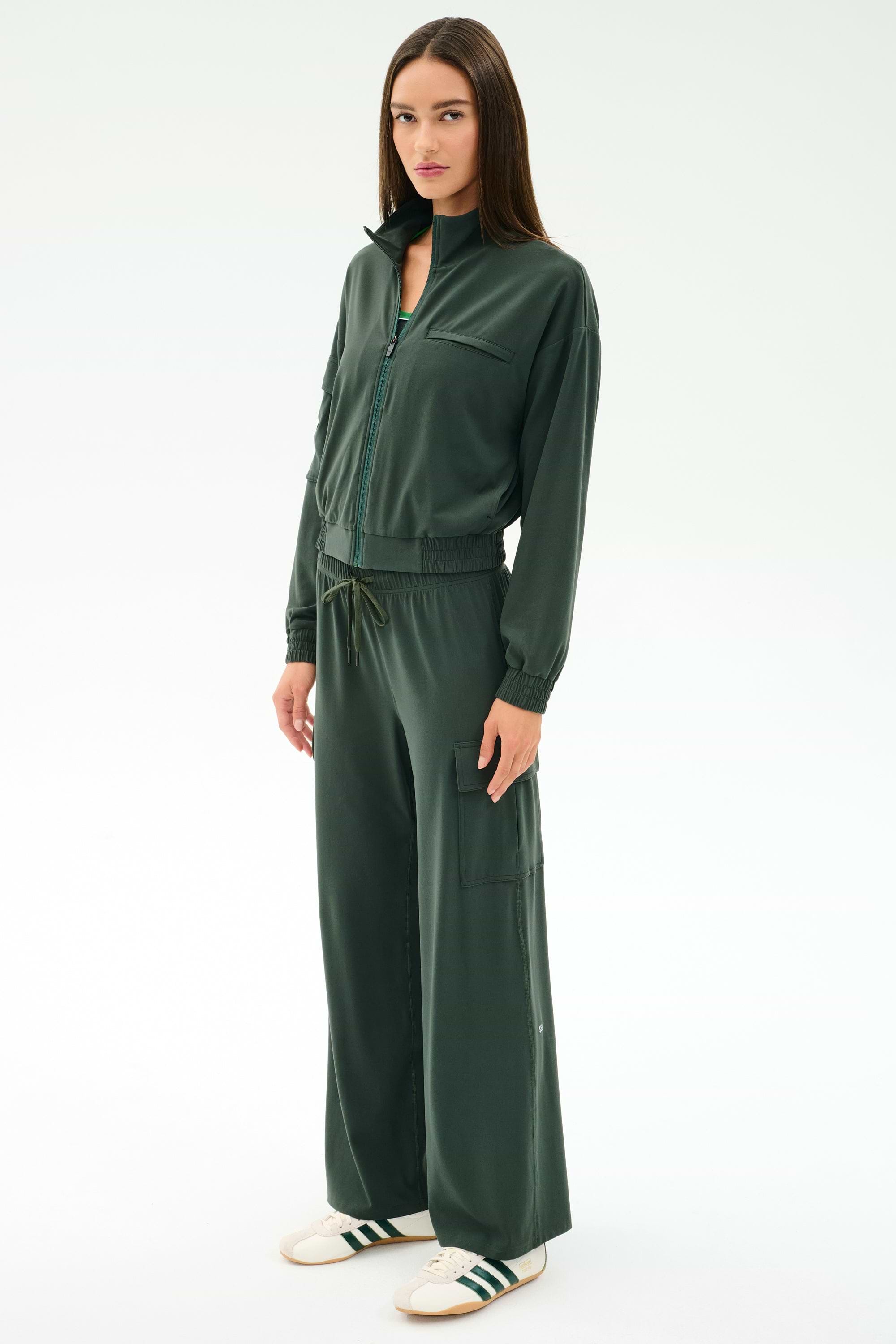 A woman stands in a relaxed pose wearing the SPLITS59 Peaches Airweight Cargo Jacket in Military and matching wide-leg pants, paired with white sneakers against a plain light background.