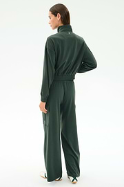 A woman stands with her back to the camera wearing SPLITS59's Alex Airweight Cargo Pant in Military, styled with a dark green top and white sneakers, on a plain white background.