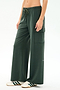 A person wears SPLITS59’s Alex Airweight Cargo Pant in Military, featuring a soft nylon blend, paired with white sneakers with green stripes, standing against a plain light background.