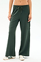 A person wearing SPLITS59 Alex Airweight Cargo Pant - Military, dark green wide-leg spandex blend pants with a side pocket, paired with white sneakers featuring green stripes, shown from waist to feet.