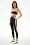 Model wears the SPLITS59 Emerson Airweight High Waist 7/8 - Black/Creme with matching sports bra and white sneakers, posed against a plain white background.