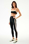 Woman wearing SPLITS59 Scottie Airweight Bra - Black/Creme and black leggings with white sneakers, standing against a plain white background.