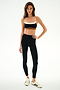 Woman in a studio wears the Emerson Airweight High Waist 7/8 - Black/Creme by SPLITS59, paired with a black and white spandex sports bra and white Adidas sneakers against a white background.