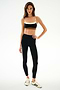 Woman stands against a plain background wearing the SPLITS59 Scottie Airweight Bra - Black/Creme, black high-waisted leggings, and white Adidas sneakers with black stripes.