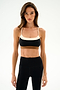 A woman models the SPLITS59 Scottie Airweight Bra - Black/Creme with high-waisted black leggings against a plain white background.