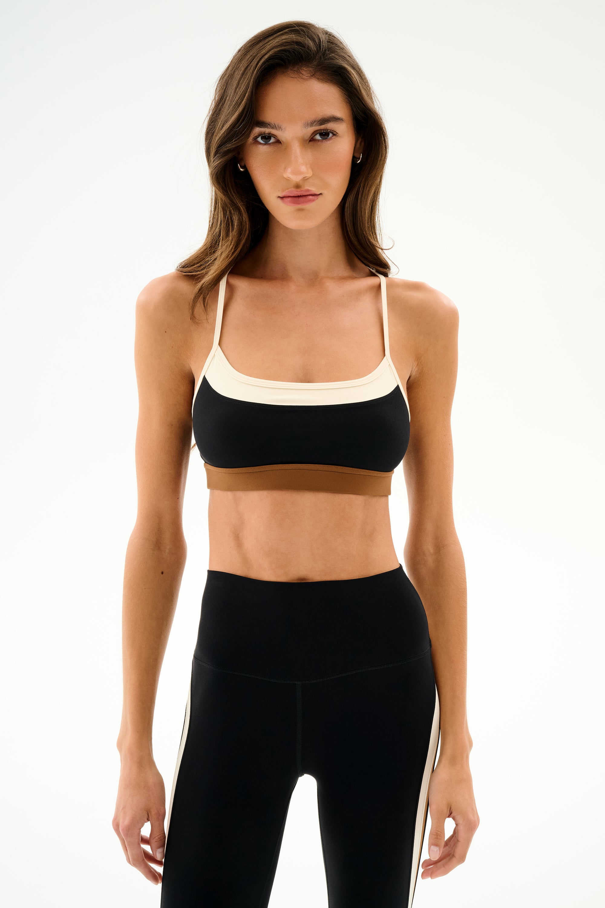 A woman models the SPLITS59 Scottie Airweight Bra - Black/Creme with high-waisted black leggings against a plain white background.